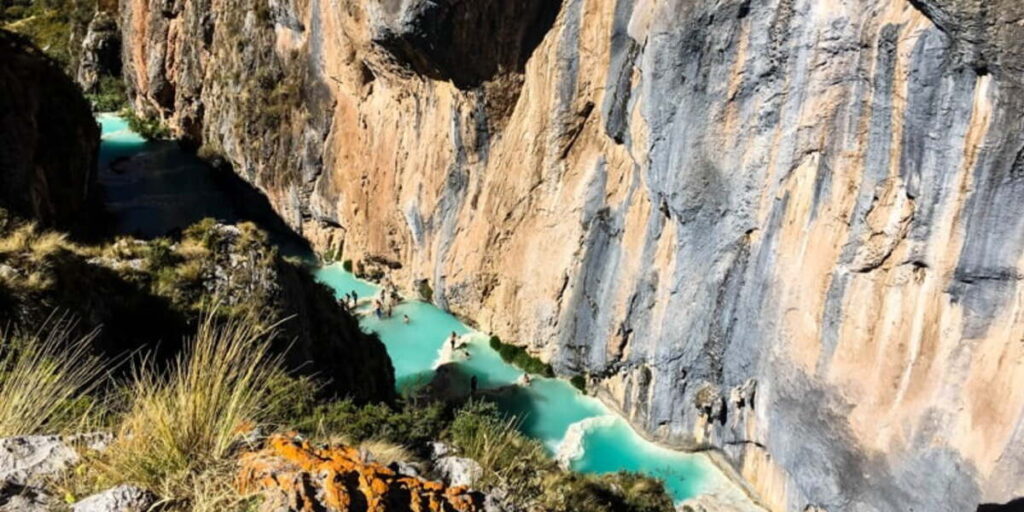 People bathing in turquoise pools nestled between steep canyon walls and lush vegetation in Millpu, Ayacucho.