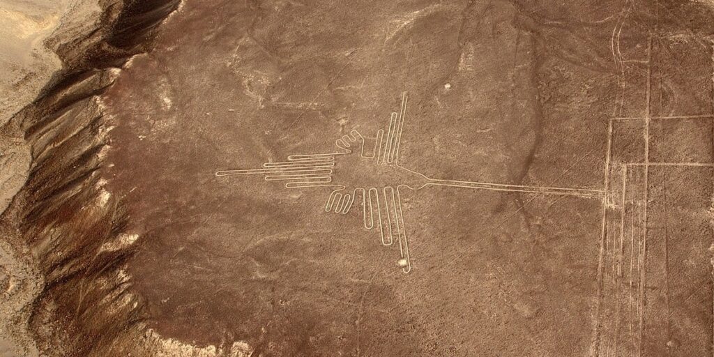 A large hummingbird geoglyph etched into the desert floor, with long, straight lines forming wings and a slender beak visible from an aerial perspective.