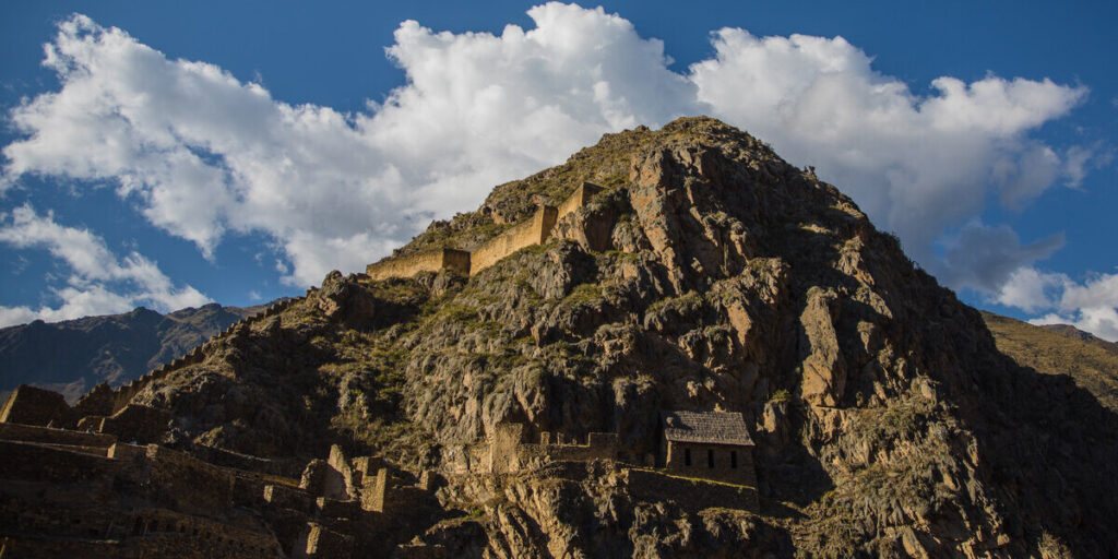 Ancient Inca storage structures known as Pinkuylluna cling to the side of a steep, rocky mountain above Ollantaytambo in the Sacred Valley.