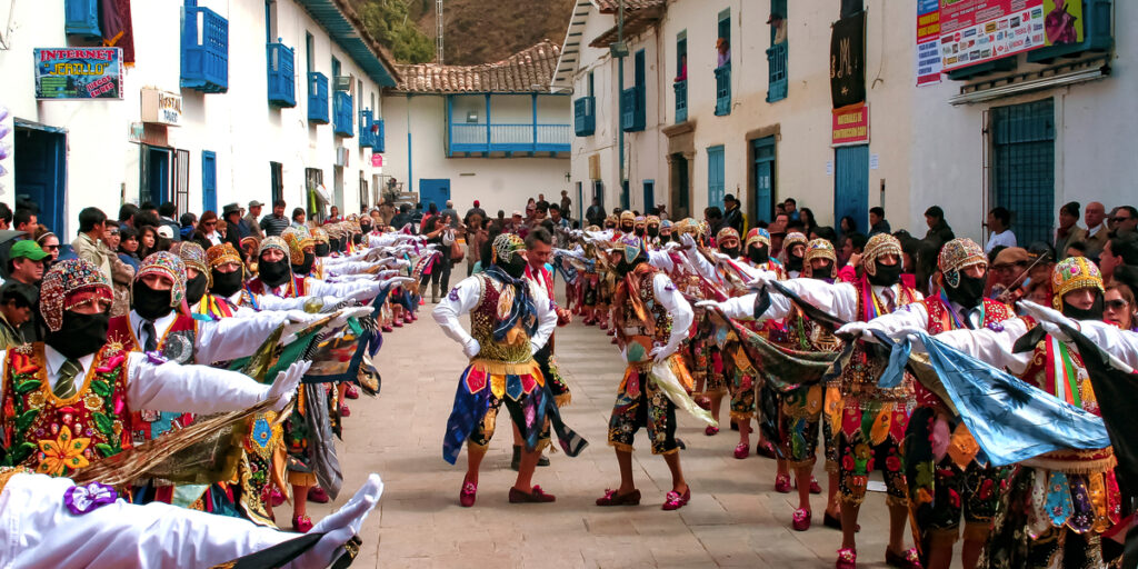 Masked dancers in vibrant, multicolored costumes perform during the Paucartambo Festival in Peru, as crowds gather around.