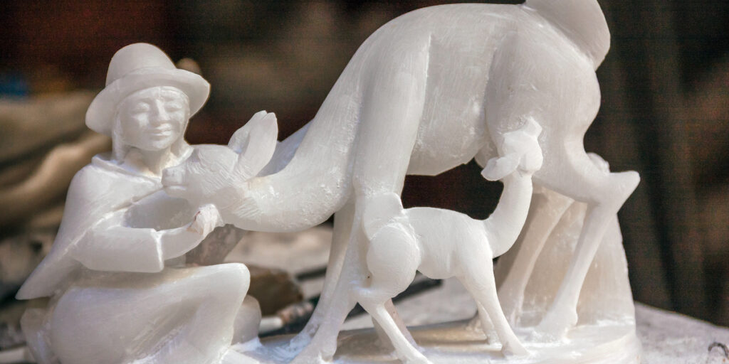 A delicate Huamanga stone sculpture of a kneeling woman gently caressing a vicuña, with a baby vicuña standing beside them