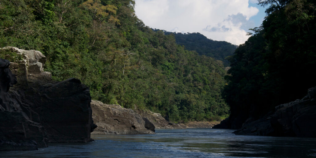 Steep, forest-covered cliffs rise dramatically on either side of the Urubamba River at Pongo de Mainique, where turbulent waters rush through the narrow canyon under misty skies.