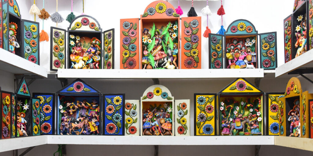 Several colorful retablos ayacuchanos arranged for sale, each featuring intricate miniature scenes inside brightly painted wooden boxes.
