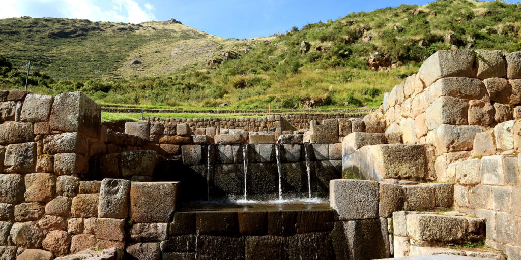 Close-up of a stone water fountain at Tipón, with clear water flowing through Inca-built channels in a carefully carved stone structure.
