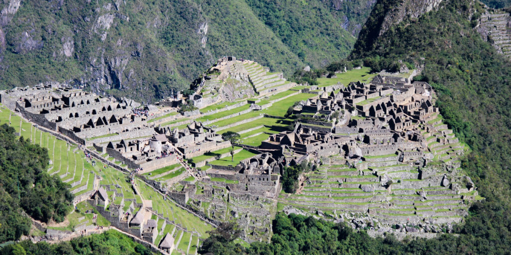 Panoramic view of Machu Picchu from Intipunku, showing the entire archaeological site nestled among lush green terraces and steep Andean slopes.