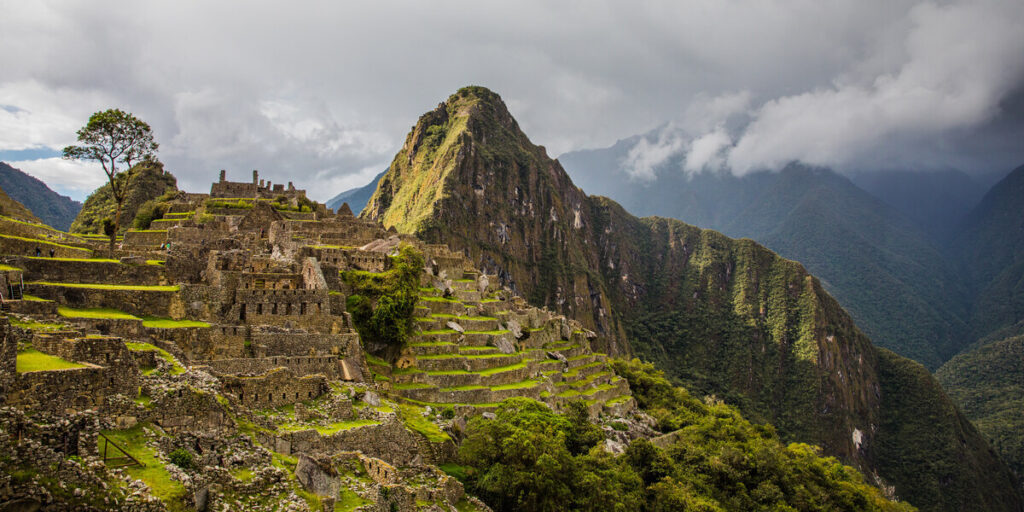A panoramic view of the ancient stone ruins of Machu Picchu, showcasing its terraced slopes, temples, and precisely crafted walls nestled high among the green Andean mountains.