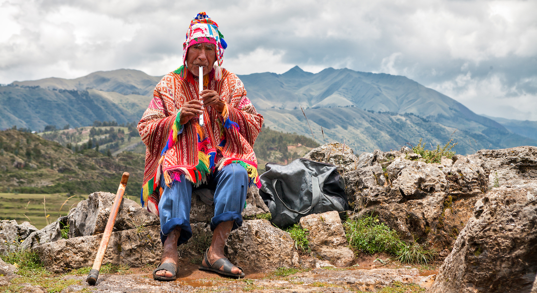 An elderly Quechua man playing a flute in the countryside.
