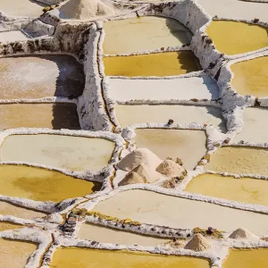A close-up view of the Maras Salt Mines, showing the geometric, terraced evaporation ponds in shades of white and yellow.