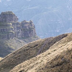 Two hikers trek on a narrow path towards the horn-shaped fortress of Waqrapukara, set on a dramatic cliff in the Peruvian Andes.