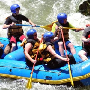 A group of people in helmets and life vests laugh and paddle together in a blue raft on a white-water river in Peru.