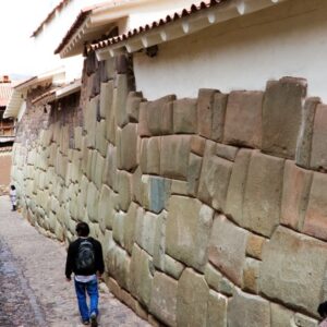 A person walks alongside an ancient Inca stone wall in a narrow street in Cusco, Peru.
