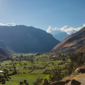View of the Sacred Valley from stone ruins, looking down on green fields and a village surrounded by towering Andes mountains.