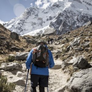 Hikers trek on a rocky path toward the snowy Salkantay Peak under a blue sky.
